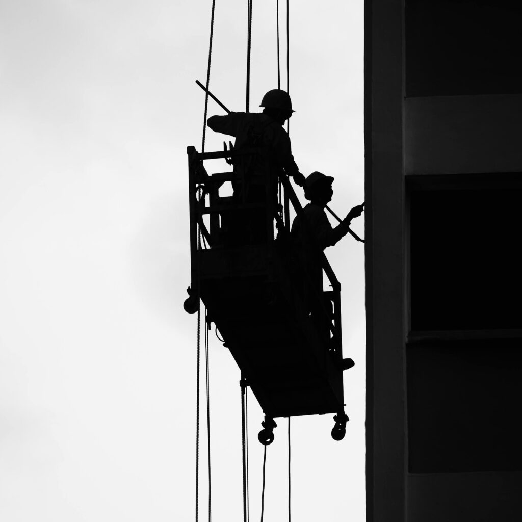 Two workers silhouetted on a suspended scaffold against a building facade.