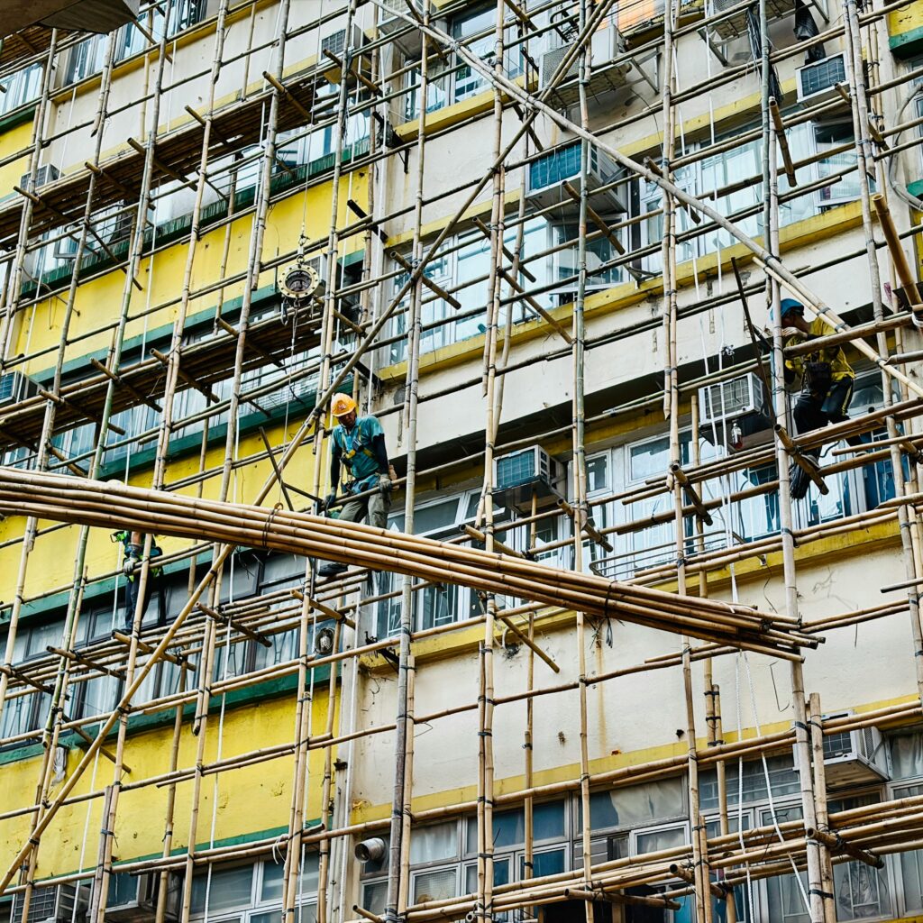 Builders working on bamboo scaffolding on a colorful building exterior.